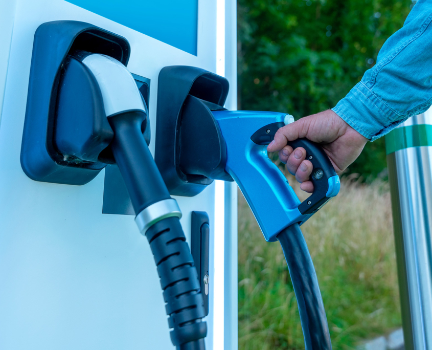 Hand Holding Pump At Ev Charging Station